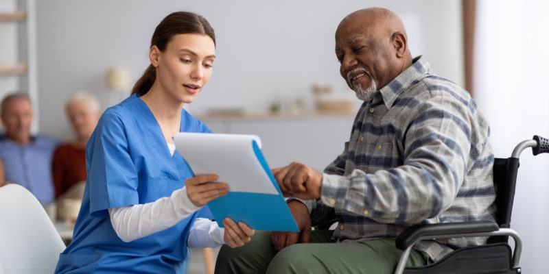 nurse helping elderly man in wheelchair with paperwork