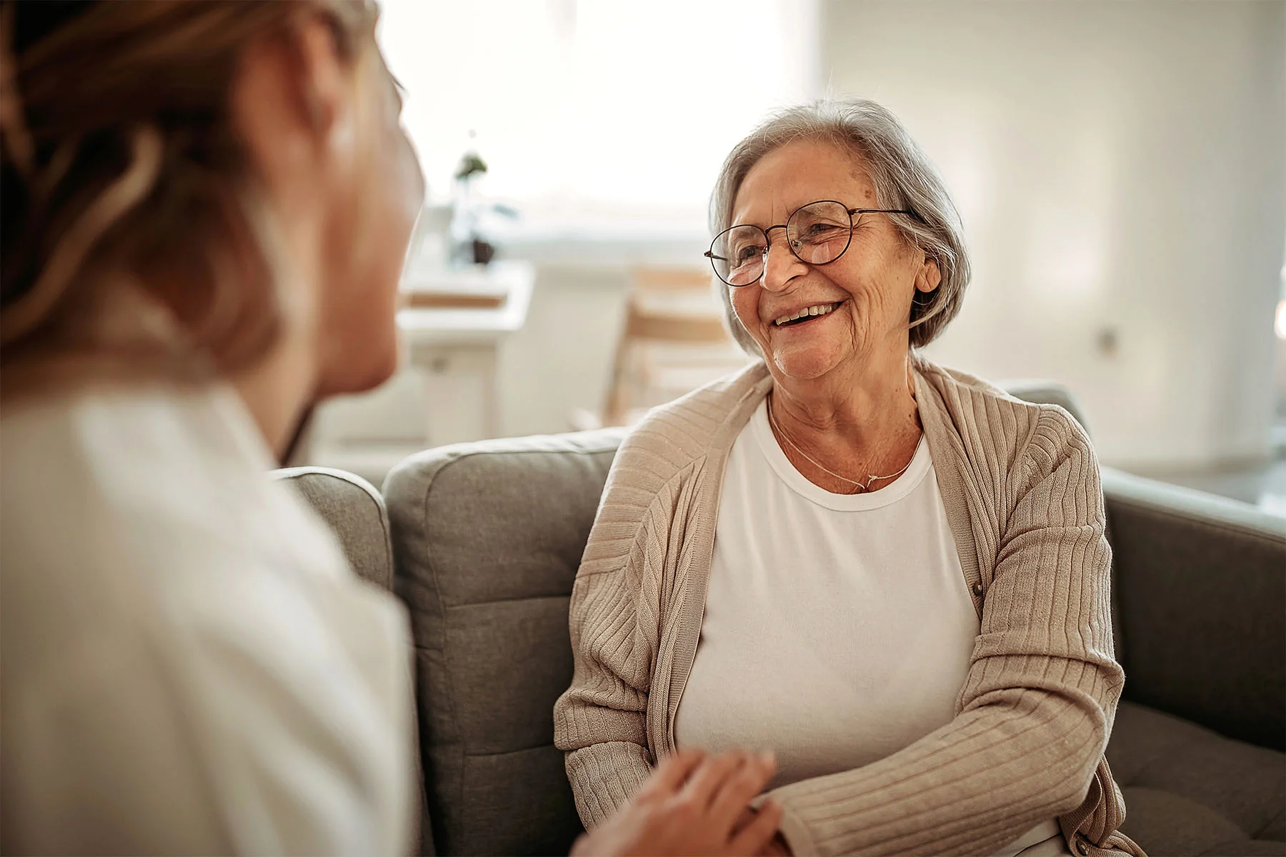 Senior smiling at caretaker comfortable on couch